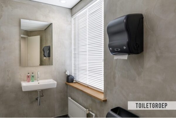 Moderne toiletruimte aan de Baarnsche Dijk met een wandwastafel, spiegel, papierenhanddoekdispenser en raam met jaloezieën.